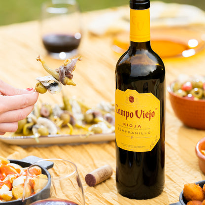 Bottle of Campo Viejo Rioja Tempranillo wine on a table with food and a glass.