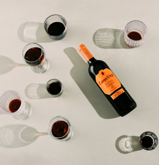 Bottle of Campovida wine with six glasses filled with red wine on a light gray background