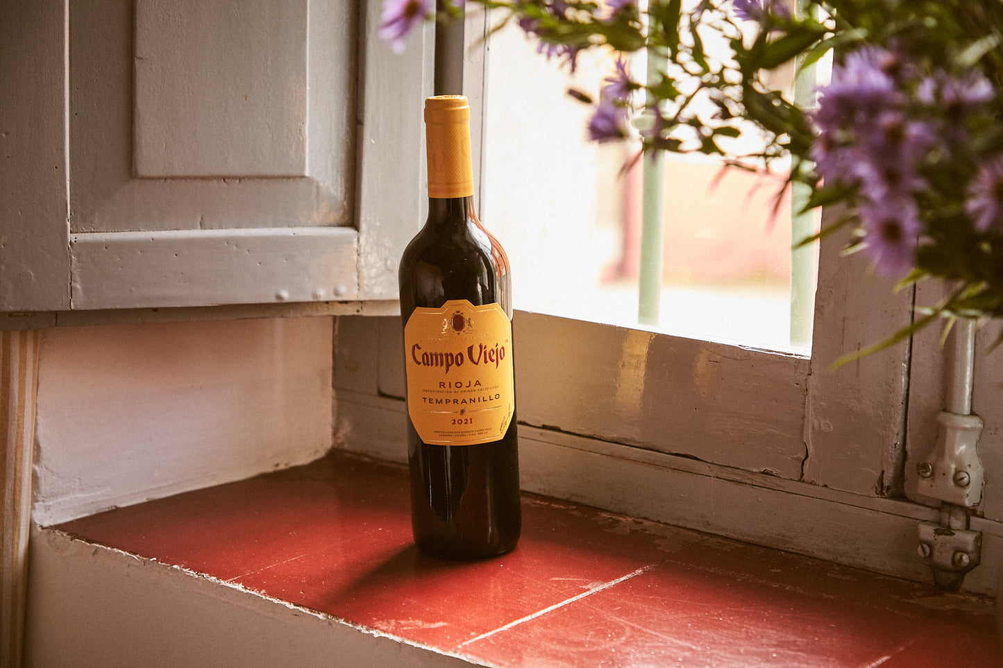 Bottle of Campo Viejo wine on a wooden surface with flowers in the background