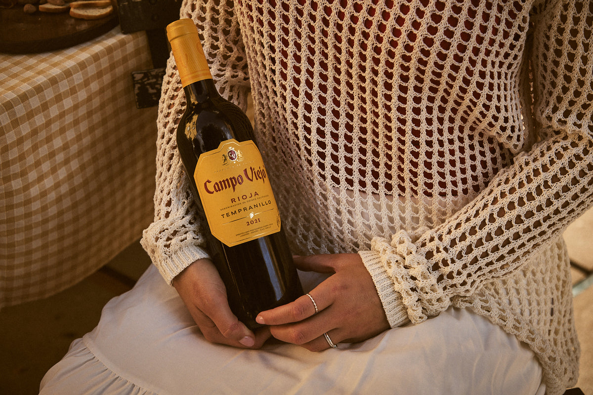 Person holding a bottle of Campo Viejo wine with a checkered tablecloth in the background
