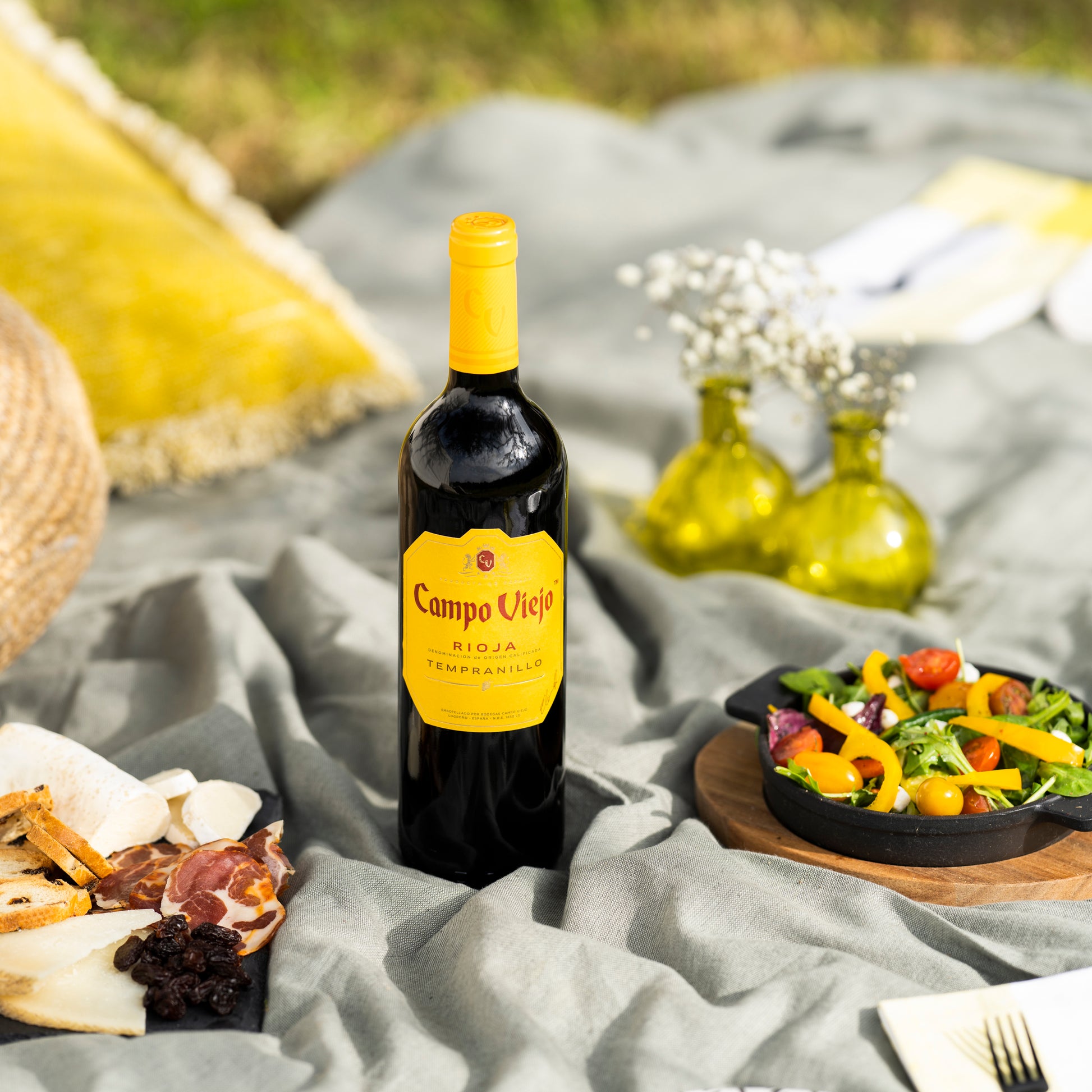 Campo Viejo Rioja wine bottle on a picnic blanket with food and flowers