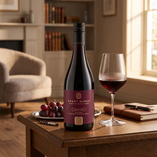 Bottle of Grant Burge wine with a glass on a wooden table in a cozy room.
